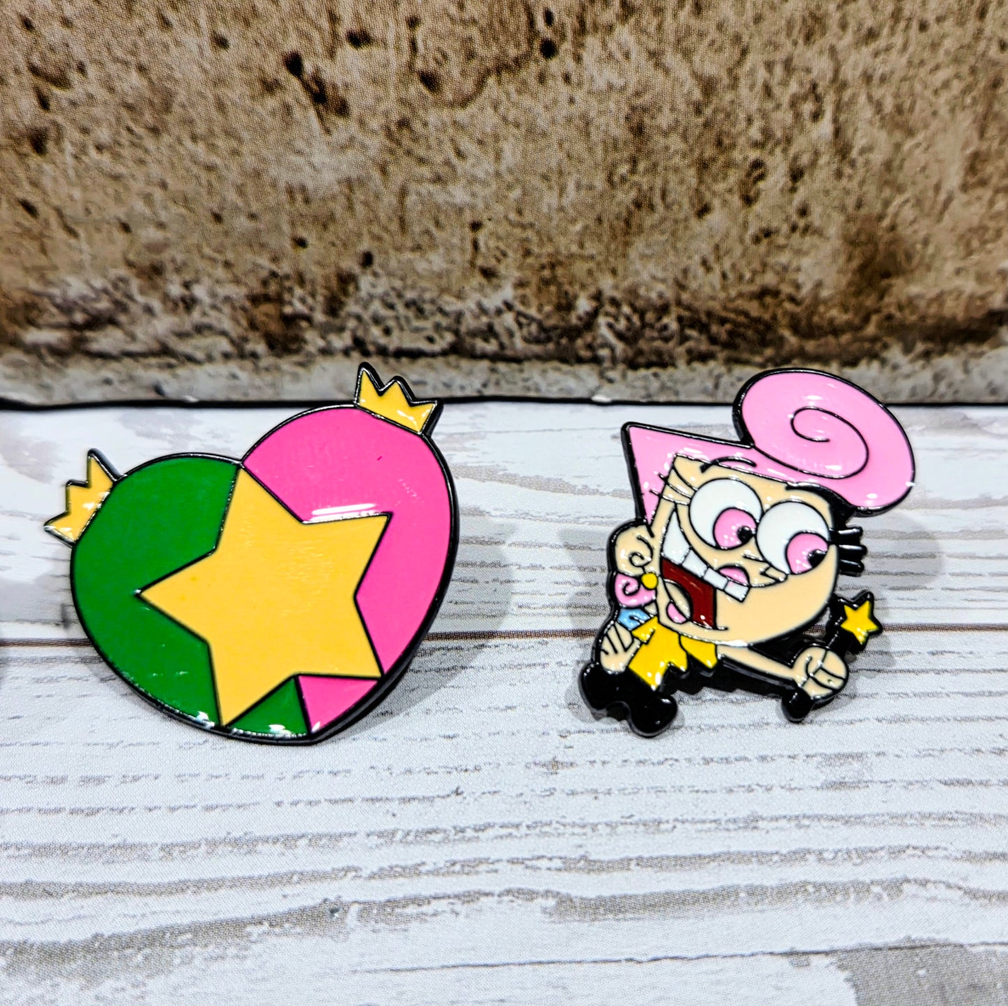 Enamel pins: green-yellow star-heart and pink-hooded Wanda character.