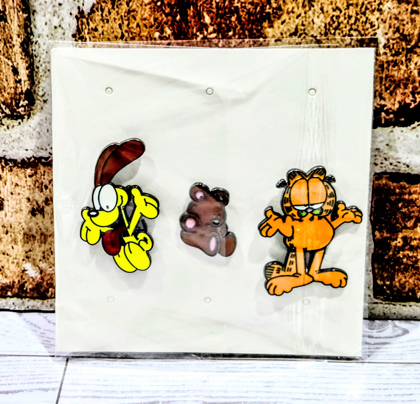 Three enamel character pins on a white pouch: yellow dog, brown bear, orange cat