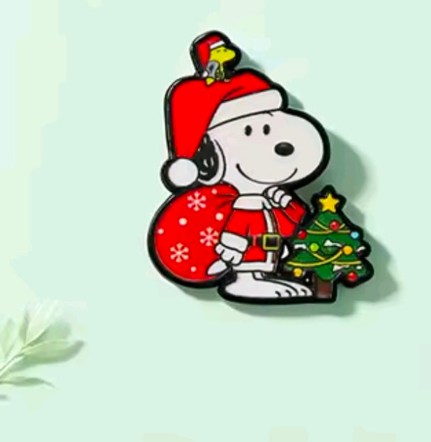 Snoopy Christmas enamel pin with Santa hat, holding Christmas tree and gifts sack