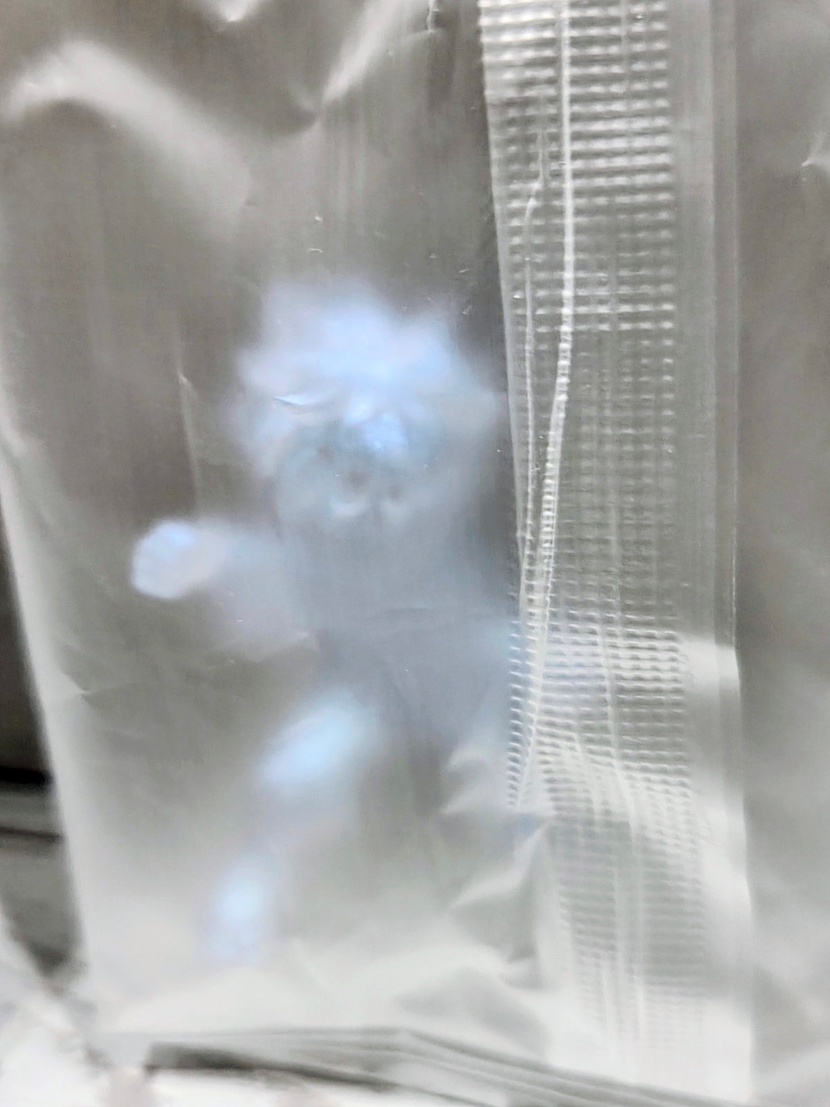 Clear plastic packaging sleeve with pale blue shimmer mini figure visible through plastic