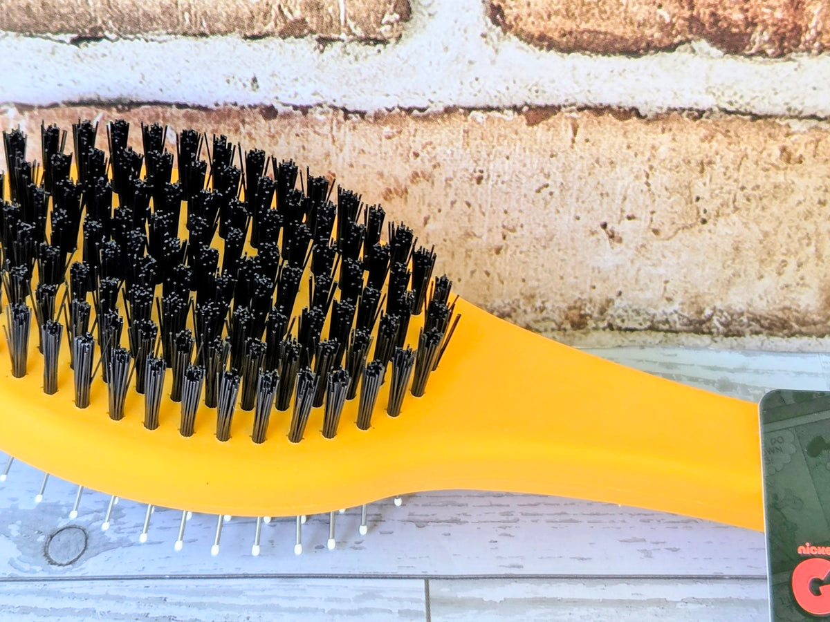 Yellow Garfield grooming brush with black bristle head and hanging packaging tag