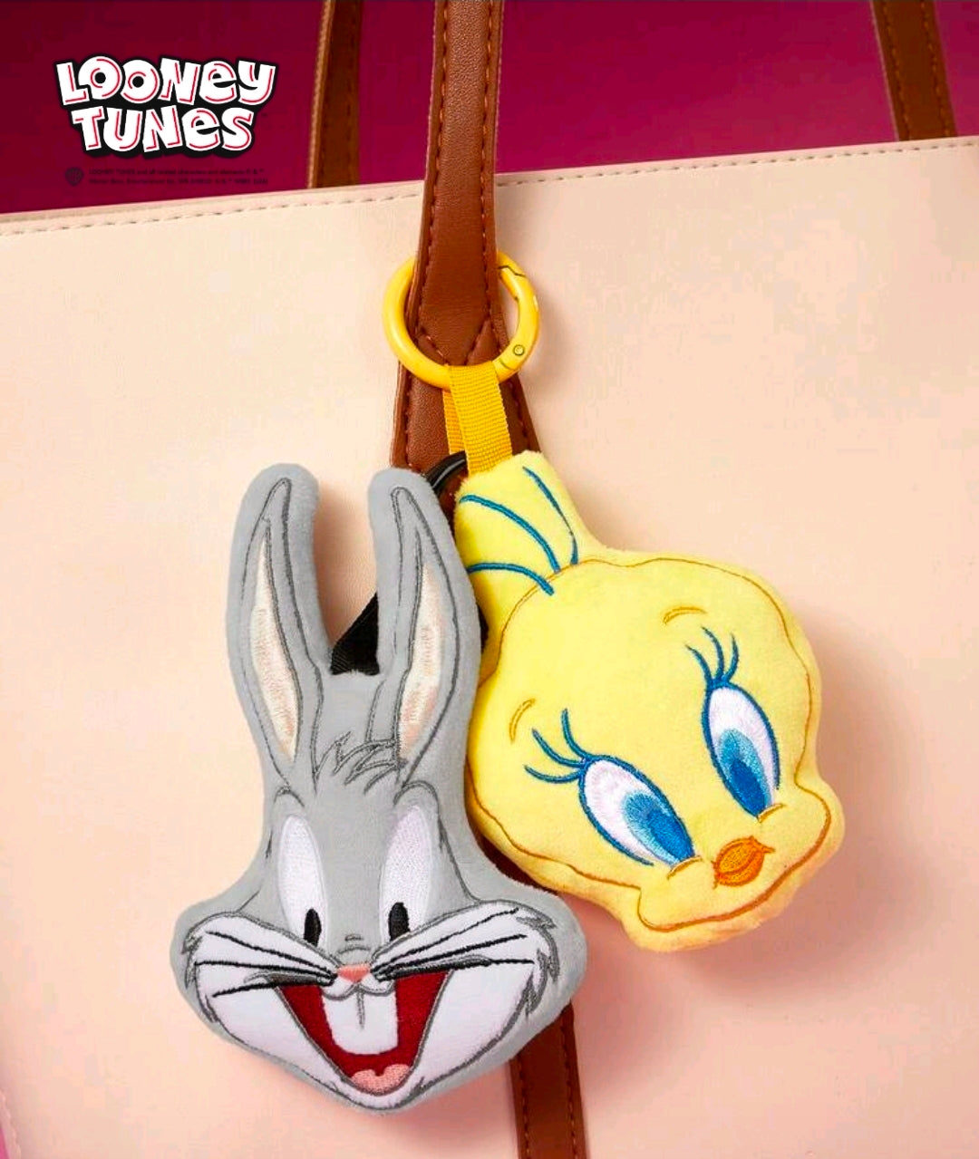 Gray plush rabbit face keychain charm with black loop on bag strap; with yellow bird charm