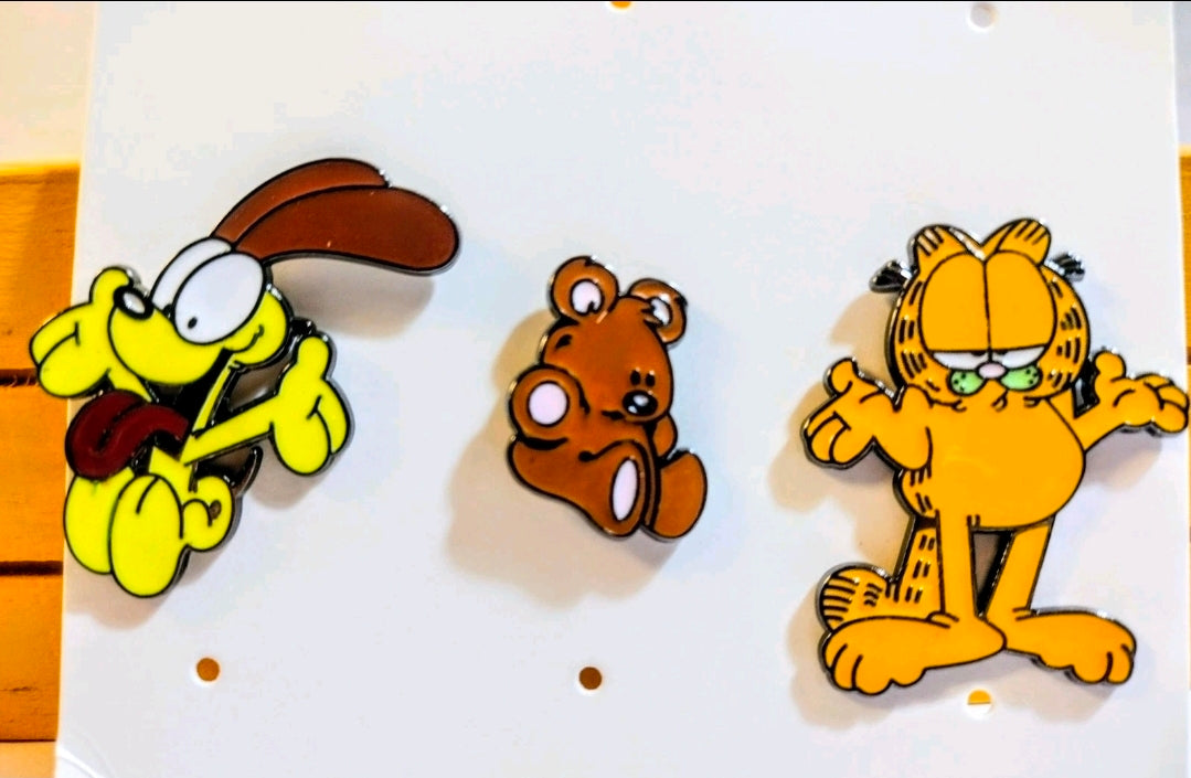 Three enamel character pins on white card: yellow dog, brown bear, orange cat