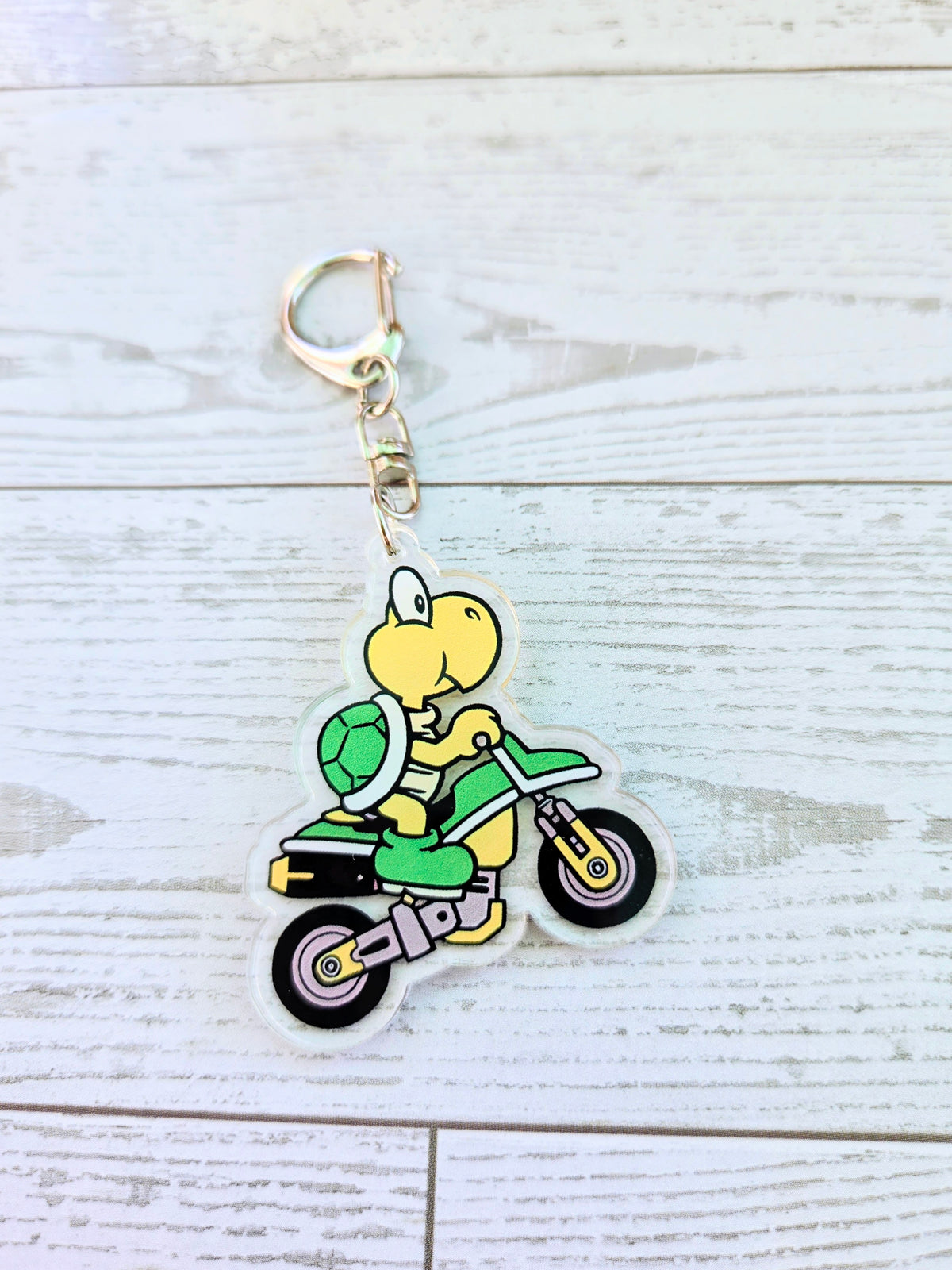 Acrylic keychain featuring Koopa Troopa riding a small green scooter