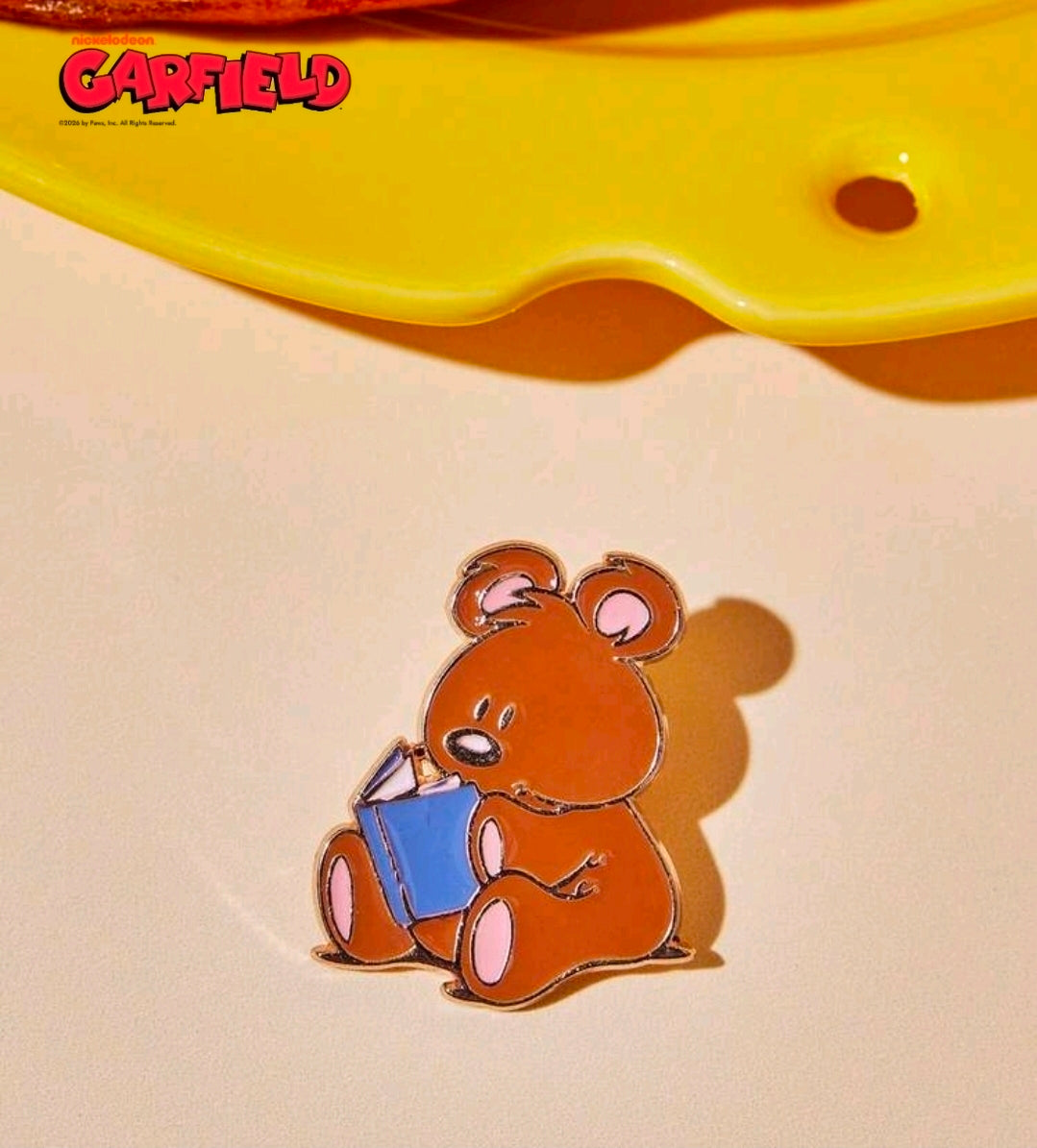 Enamel character pin of a brown bear holding a blue gift, gold-outlined