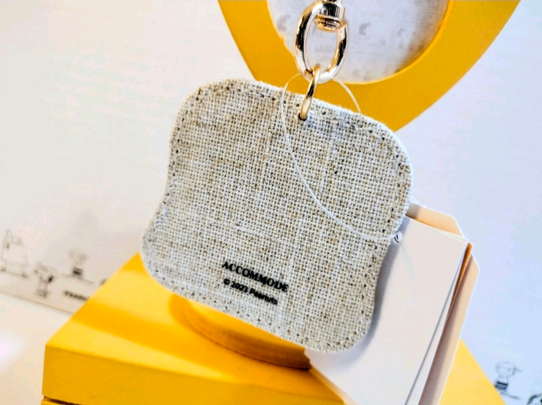 Grey fabric keychain pouch with gold keyring, marked Accommode