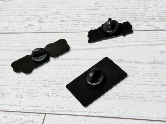 Enamel pin backs with two black metal pin posts and one flat square backing.