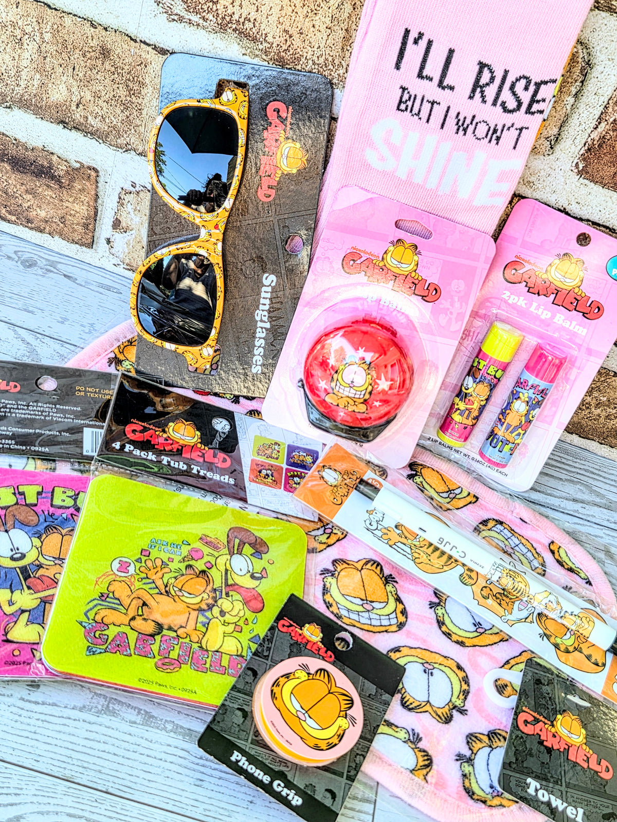 Garfield self-care bundle: pink socks with 'I'll Rise But I Won't Shine' and sunglasses.