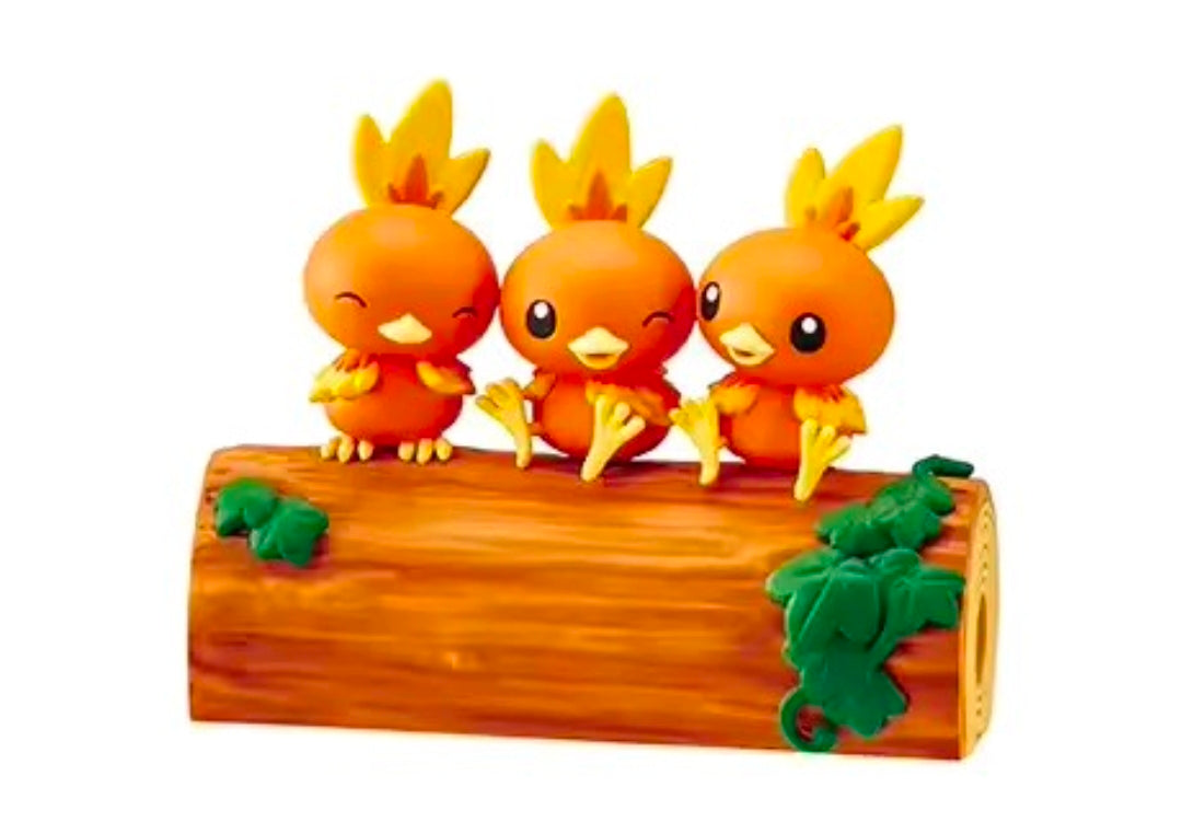Three orange Torchic figures on a brown log with green clumps and pink accents.