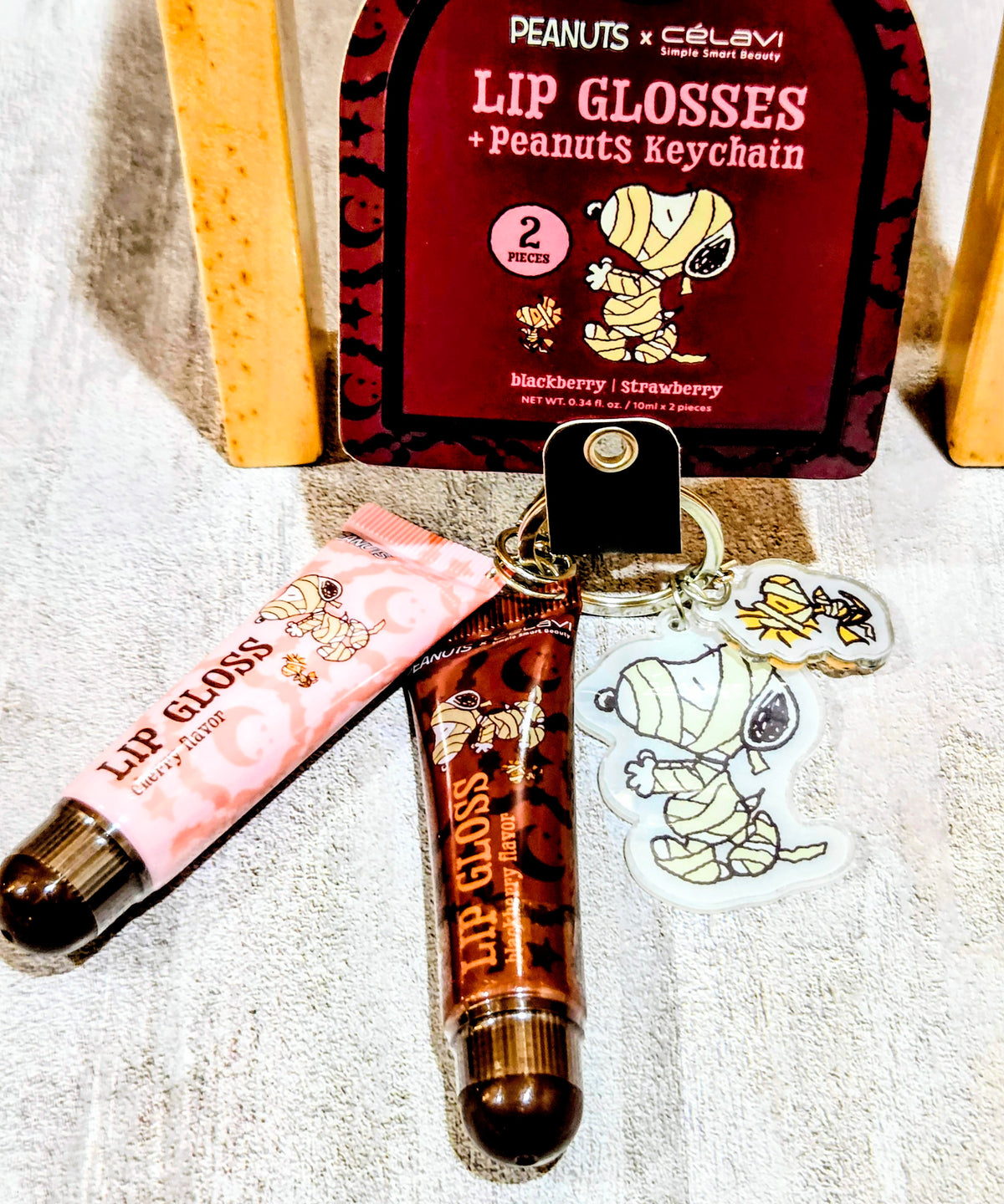 Two lip gloss tubes with Peanuts keychain and sticker charms on display