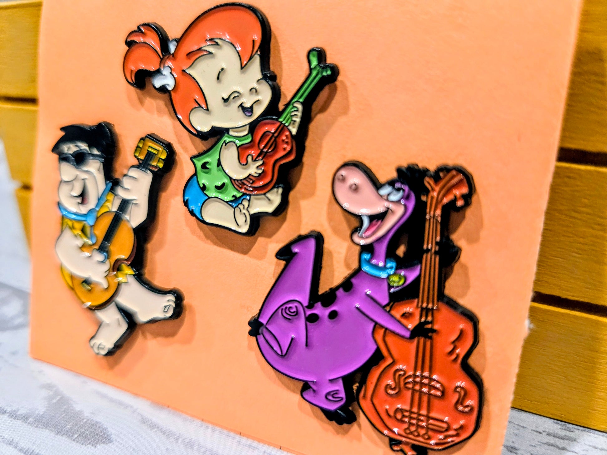 Enamel pin set featuring Fred, Pebbles, and Dino with instruments