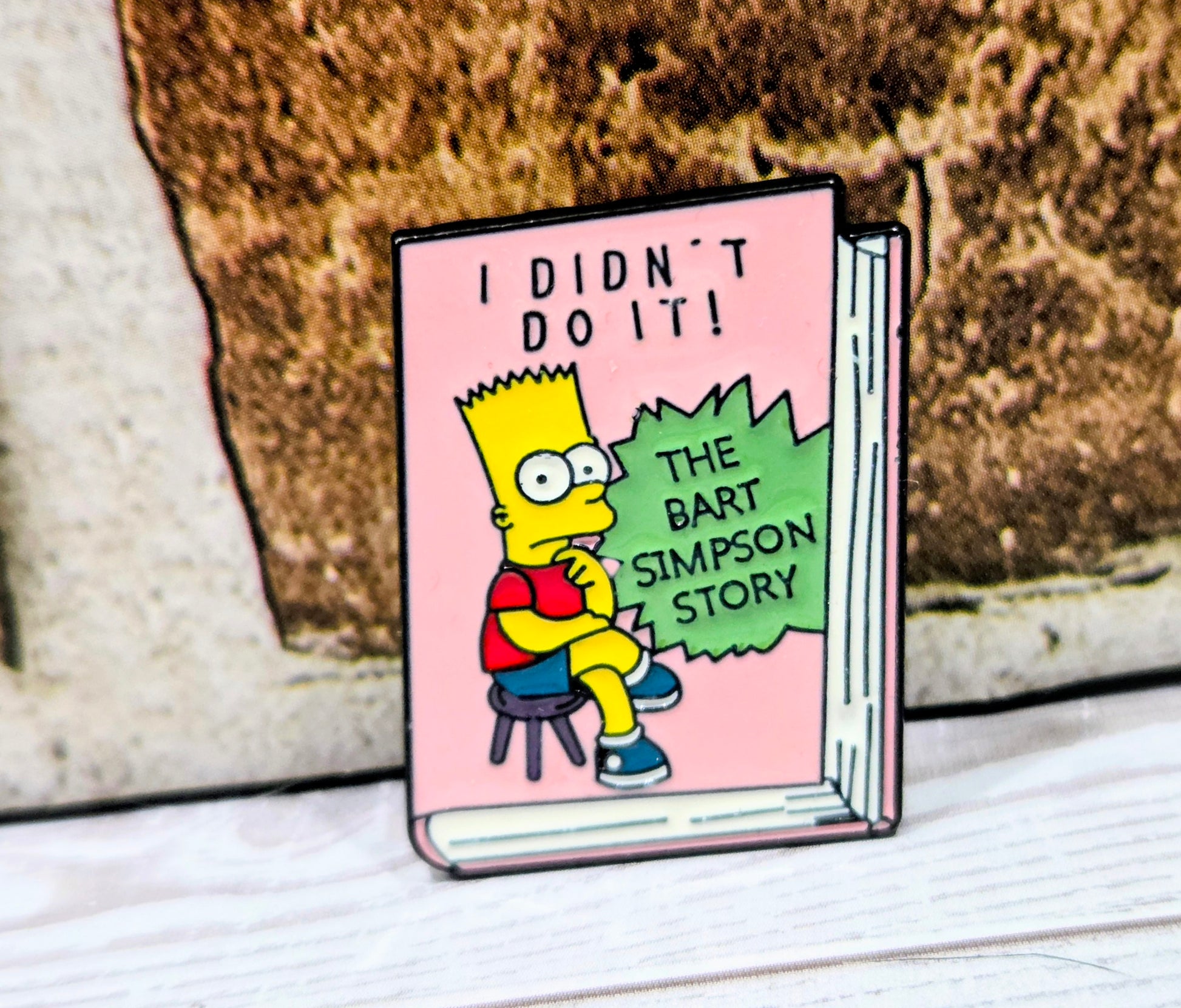 pink book-shaped enamel pin with Bart character and speech text 'I DIDN'T DO IT!'