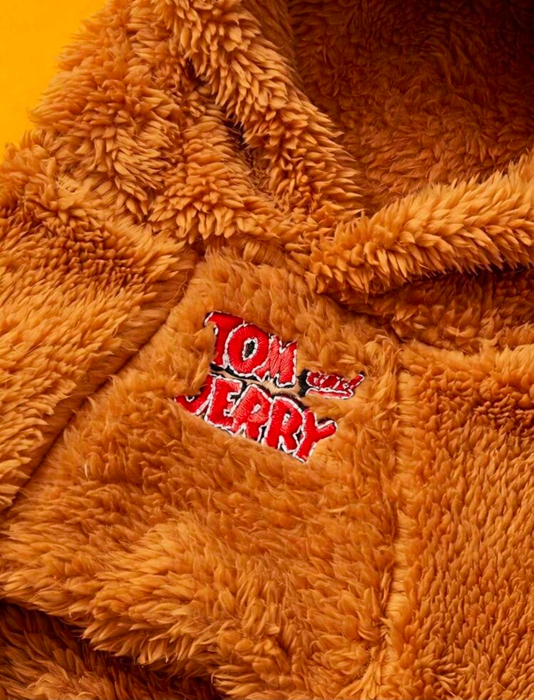 Orange-brown plush dog hoodie with mouse ears and red logo patch at chest