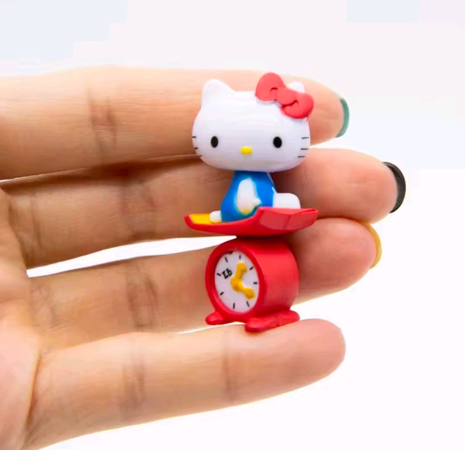 Hello Kitty mini figure standing on a red alarm clock with blue dress and green bow