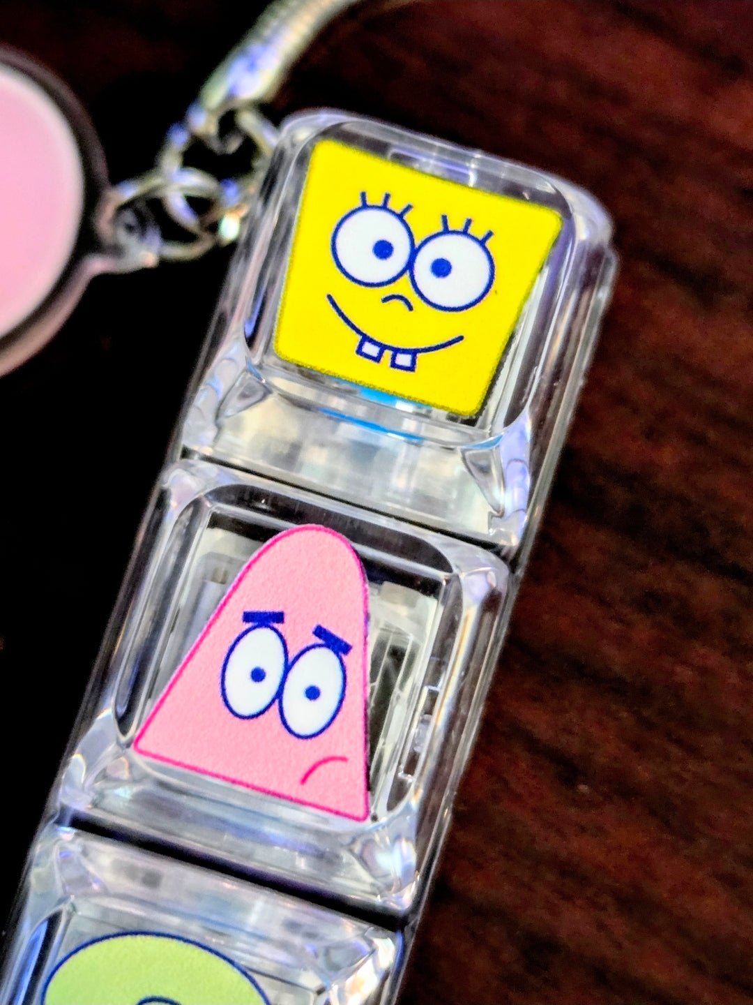 Clear acrylic keyboard fidget keychain close-up, showing SpongeBob and pink character faces