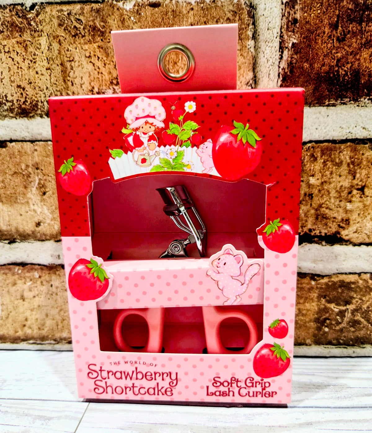 Strawberry-themed eyelash curler retail box with open tray and metal clamp