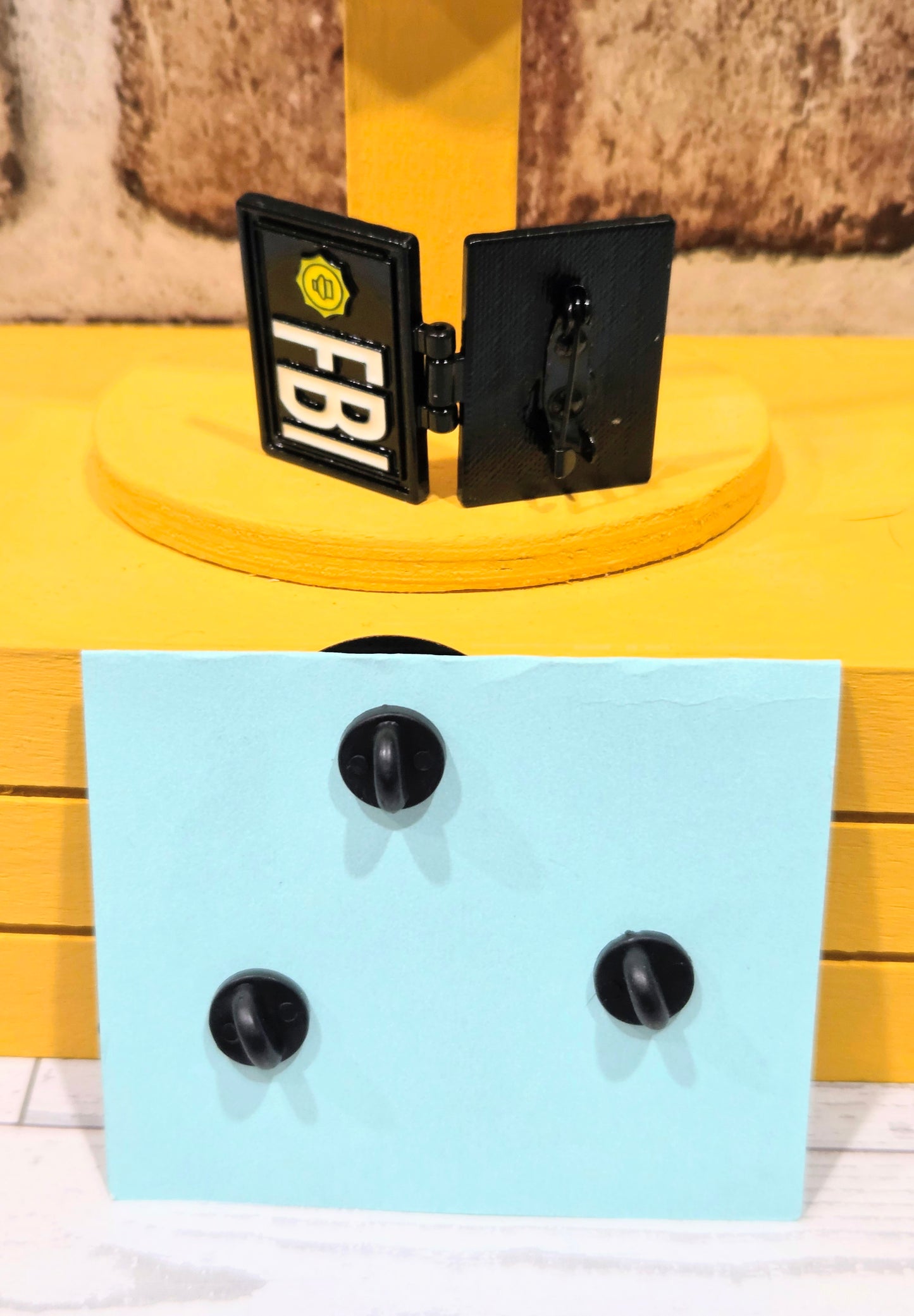 Enamel pin backs on display card, showing black clutch posts and hinged pieces.