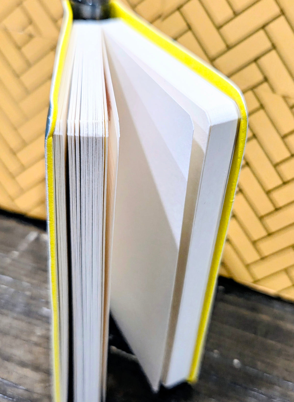 White pocket field notebook with yellow-edged faux leather binding and visible stacked pages