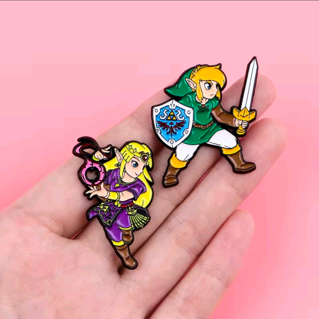 Two enamel pins on a hand: Zelda in purple and Link in green with sword and shield