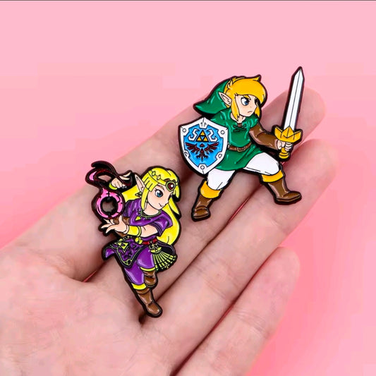Two enamel pins on a hand: Zelda in purple and Link in green with sword and shield