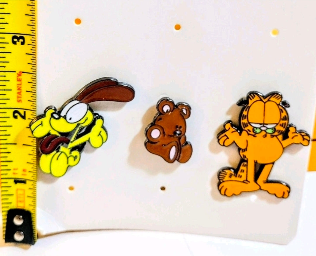 Three enamel character pins on display card next to a measuring ruler edge